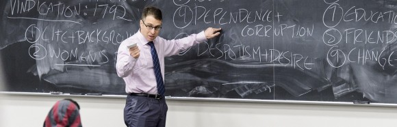 Professor gestures at chalk board.